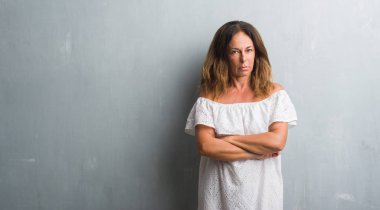 Gri grunge duvar şüpheci ve gergin duran, çapraz kolları olan yüzündeki ifade onaylamayan orta yaş İspanyol kadın. Negatif kişi.