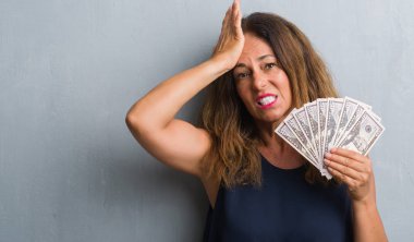Baş, el ile vurguladı dolar tutan gri grunge duvarın üzerinden duran orta yaş İspanyol kadın şok utanç ve sürpriz suratla, öfkeli ve sinirli. Korku ve hata için üzgün.