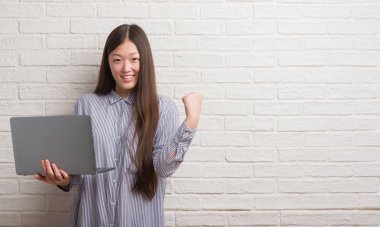 Duygu tezahürat Genç Çinli kadın gurur çığlık ve zafer ve başarı çok heyecanlı, kutluyor dizüstü kullanarak tuğla duvar üzerine