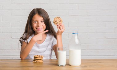 Süt içme ve çikolata bisküvi el ve parmak ile işaret çok mutlu yemek masada oturan genç İspanyol çocuk