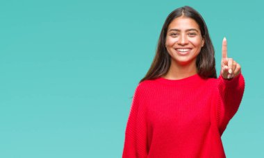 Ve parmak gülümseyen süre bir numara ile kendinden emin ve mutlu yukarıyı gösteren izole arka plan üzerinde kış kazak giyen genç güzel Arap kadın.