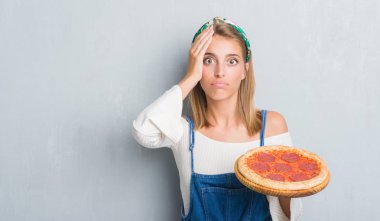 Güzel genç kadın baş, el ile vurguladı biberli pizza yeme grunge gri duvar yüzünden şok utanç ve sürpriz suratla, öfkeli ve sinirli. Korku ve hata için üzgün.