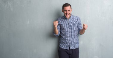 Gri grunge duvar kutluyor üzerinde beyaz delikanlı şaşırttı ve başarı için kaldırdı kollarını açarak hayret ve gözleri açık. Kazanan kavramı.