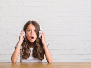 Kulaklıklar bir sürpriz yüz, korkuyor ve heyecanlı korku ifadesi ile şok korkmuş giyen masada oturan genç İspanyol çocuk