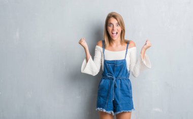 Grunge gri duvar kutluyor üzerinde duran güzel genç kadın şaşırttı ve başarı için kaldırdı kollarını açarak hayret ve gözleri açık. Kazanan kavramı.