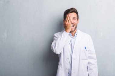 El yüz ve sürpriz duygu kendinden emin gülümseme ile tek gözü kaplayan gri grunge duvar giyen üzerinde profesyonel yakışıklı genç beyaz ceket.