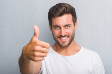 Ok işareti, başparmak ile parmak, mükemmel işareti yapıyor kocaman bir gülümseme ile mutlu gri grunge duvarın üzerinden yakışıklı genç
