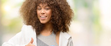 Afro-Amerikan fitness kadın holding su şişesi ok işareti, başparmak ile parmak, mükemmel işareti yapıyor kocaman bir gülümseme ile mutlu