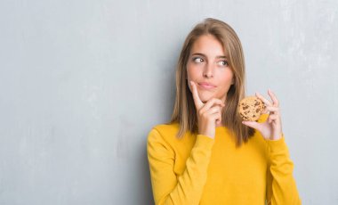 Çikolatalı bisküvi ciddi bir yüz düşünme hakkında soru, çok karışık fikir yeme grunge gri duvar güzel genç kadın