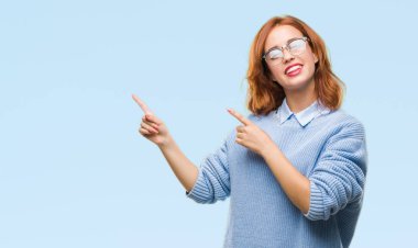 İzole arka plan gülümseyen ve iki elleri ve parmakları ile tarafına işaret kamera bakarak kış kazak giyen genç güzel kadın.