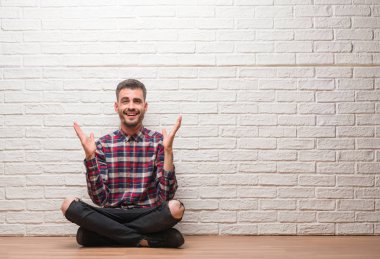 Kocaman bir gülümseme ile çığlık ve ellerini kaldırdı zaferini kutluyor beyaz tuğla duvar çok mutlu ve heyecanlı, kazanan ifade üzerinde oturan genç yetişkin adam