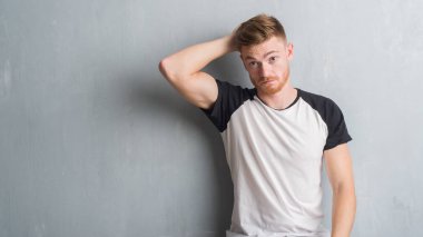 Genç Kızıl saçlı adam gri grunge duvarın üzerinden yanıltır ve soru hakkında merak ediyorum. Şüphe, kafasına el ile düşünme ile belirsiz. Dalgın kavramı.