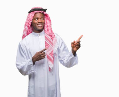 Gülümseyen ve iki elleri ve parmakları ile tarafına işaret kamera bakarak izole arka plan üzerinde geleneksel keffiyeh giyen genç Arapça Afrika adam.