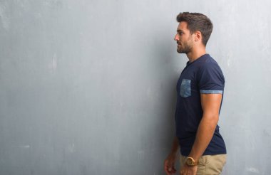 Yakışıklı delikanlı tarafına, seyir gri grunge duvarın üzerinden dinlenmek doğal yüz emin gülümseme ile pozuyla profil.
