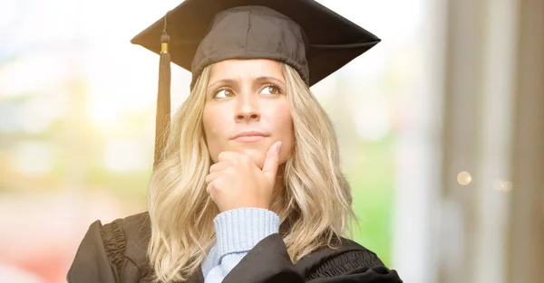 Young graduate woman thinking and looking up expressing doubt and wonder