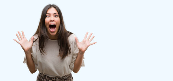 Молодая красивая латиноамериканка очень счастлива и взволнована, выражение победителя празднует победу крича с большой улыбкой и поднятыми руками
