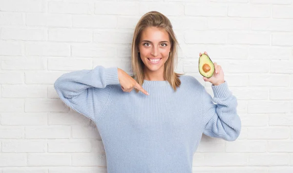 Hermosa Mujer Joven Sobre Pared Ladrillo Blanco Comiendo Aguacate Fresco —  Fotos de Stock