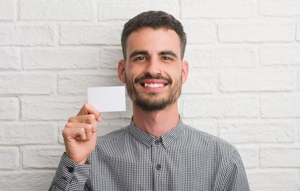 Homem Adulto Jovem Sobre Parede Tijolo Segurando Cartão Branco Com — Fotografia de Stock