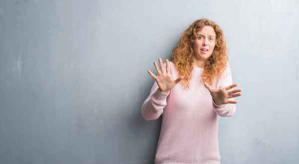 灰色垃圾墙上的年轻红头发的女人穿着粉红色的毛衣害怕和恐惧的表情停止手势 在震惊中大叫 恐慌概念 — 图库照片