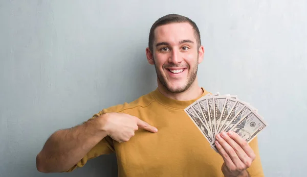 Young Caucasian Man Grey Grunge Wall Holding Dollars Surprise Face — Stock Photo, Image