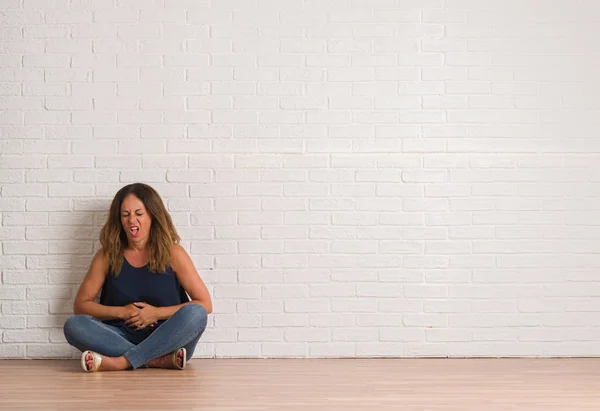 白いレンガの壁にので胃の手で床に座っている中年ヒスパニック女性消化不良 気分が悪く痛みを伴う病気 痛みの概念 — ストック写真