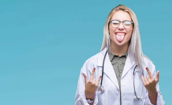 Young blonde doctor woman over isolated background shouting with crazy expression doing rock symbol with hands up. Music star. Heavy concept.