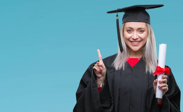 Young blonde woman wearing graduate uniform holding degree over isolated background surprised with an idea or question pointing finger with happy face, number one