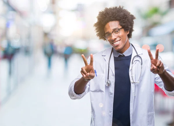 美国黑人医生在孤立的背景下微笑着看着相机 显示手指做胜利标志 第二个 — 图库照片