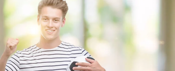 Joven Guapo Hombre Rubio Sosteniendo Pelota Fútbol Gritando Orgulloso Celebrando —  Fotos de Stock