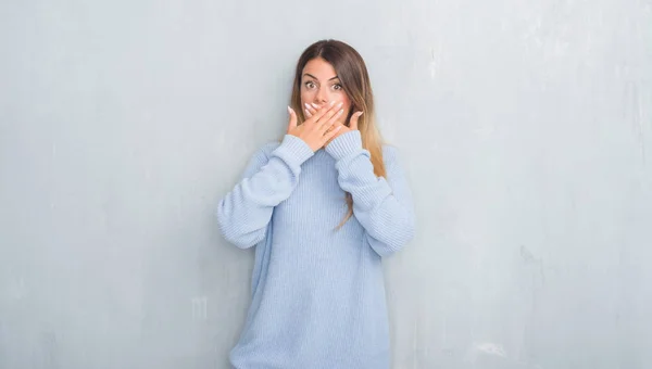 ミスのため手で口を覆っているショックを受けて冬の服装を身に着けている灰色のグランジの壁を越えて若い大人の女性 秘密の概念 — ストック写真