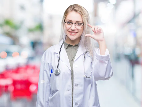 年轻的金发医生的女人在孤立的背景微笑和自信的手势与手做尺寸符号与手指 当看和相机 度量概念 — 图库照片