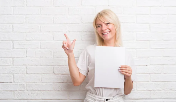 Mujer Caucásica Adulta Sobre Pared Ladrillo Blanco Sosteniendo Hoja Papel —  Fotos de Stock