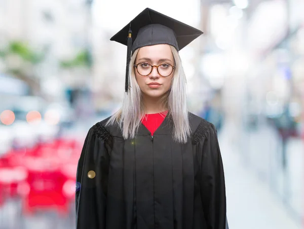 年轻的金发女子穿着毕业制服在孤立的背景下 面部表情严肃 简单而自然地看着相机 — 图库照片