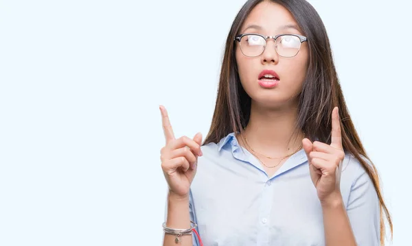 年轻的亚洲商业妇女戴着眼镜在孤立的背景下惊讶和惊讶地看着手指和举起手臂 — 图库照片