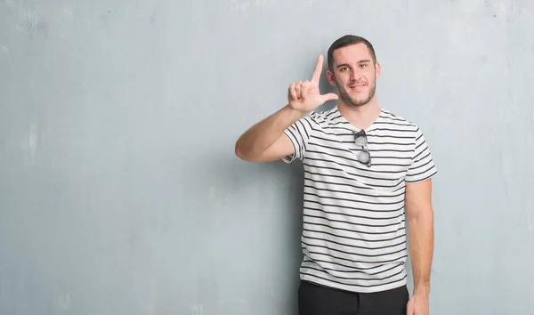 Joven Caucásico Hombre Sobre Gris Grunge Pared Mostrando Apuntando Hacia —  Fotos de Stock