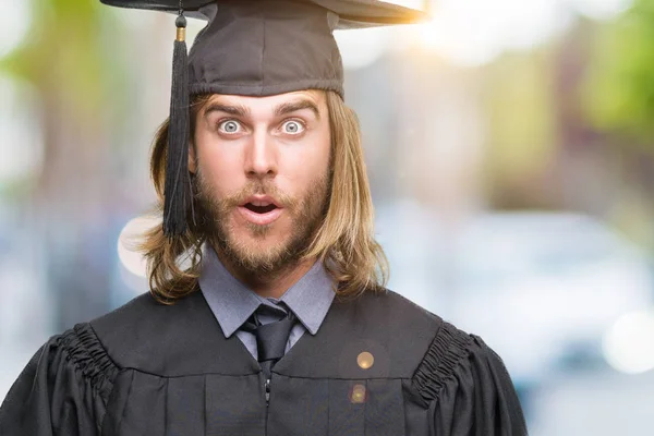 驚きの表情でショックを受けて孤立の背景の上の長い髪の若いハンサムな卒業男性恐怖し 顔を興奮 — ストック写真