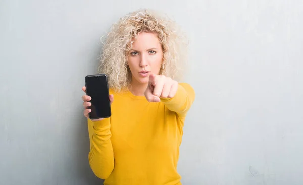 Młoda Blondynka Nad Streszczenie Szary Tło Wyświetlono Pusty Ekran Smartphone — Zdjęcie stockowe