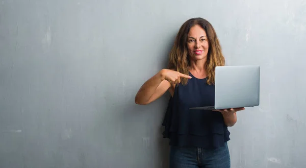 中年西班牙裔妇女站在灰色的垃圾墙使用笔记本电脑与惊讶的脸指着自己 — 图库照片
