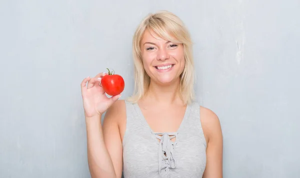 成年白种人女人在垃圾灰墙上抱着新鲜的西红柿 脸上带着一张笑脸 微笑着 露出了自信的笑容 图库图片