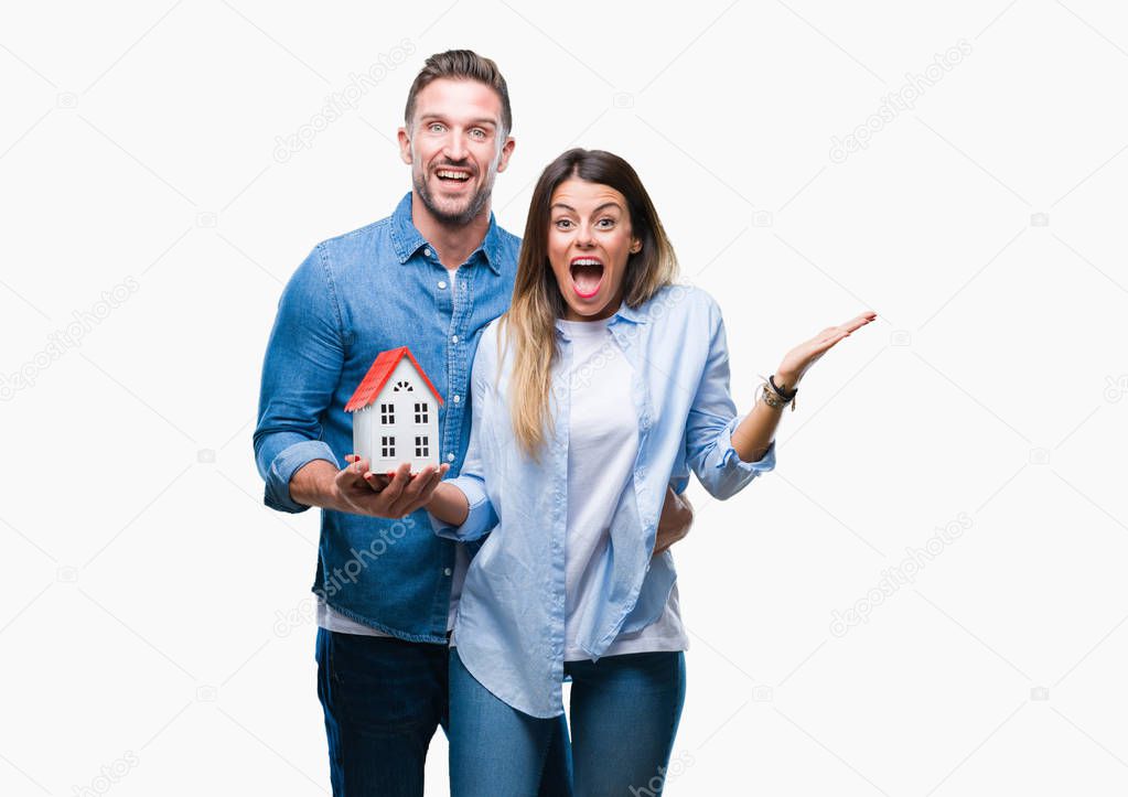 Young couple in love holding house over isolated background very happy and excited, winner expression celebrating victory screaming with big smile and raised hands