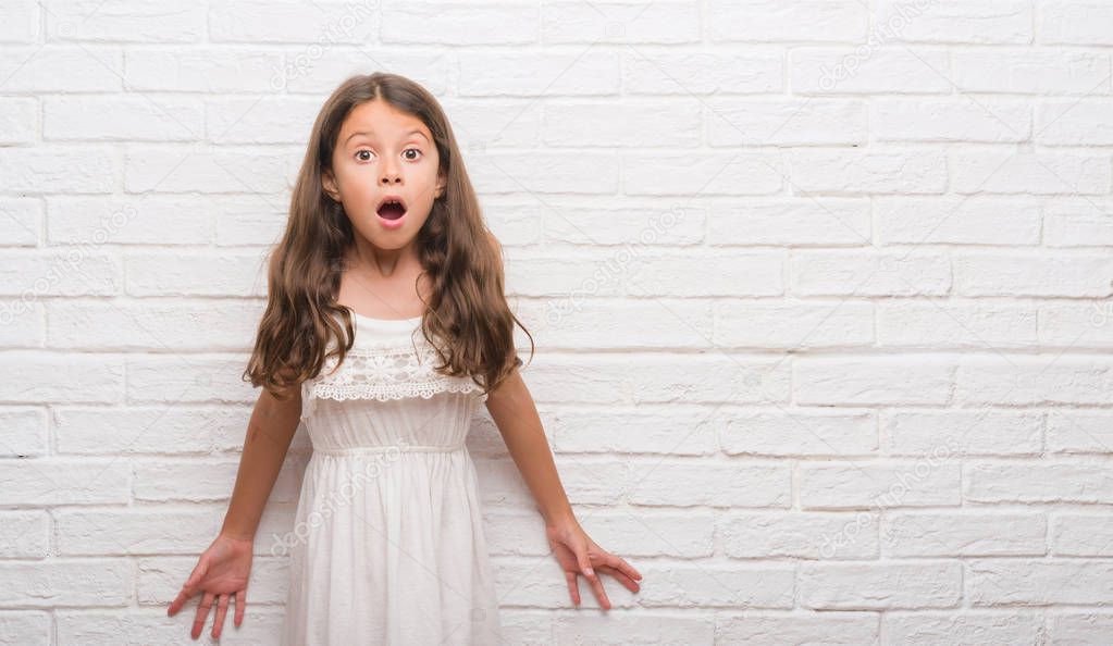 Young hispanic kid over white brick wall afraid and shocked with surprise expression, fear and excited face.