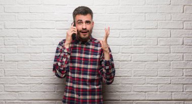 Kocaman bir gülümseme ile çığlık ve ellerini kaldırdı zaferini kutluyor beyaz tuğla duvar çok mutlu ve heyecanlı, kazanan ifade üzerinde duran telefonda konuşan genç yetişkin adam