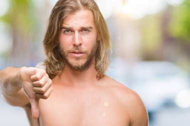 Genç yakışıklı gömleksiz adam uzun saçlı seksi vücut mutsuz ve kızgın ret gösterilen ve başparmak aşağı hareketi ile negatif seyir izole arka plan üzerinde gösterilen. Kötü ifade.