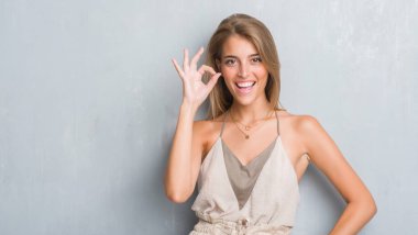 Parmak, mükemmel sembolü ile ok işareti yapıyor grunge gri duvar üzerinde duran güzel genç kadın