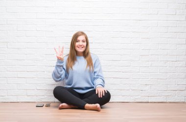 Gösterilen ve parmakları ile işaret beyaz tuğla duvarın üzerinden sonbaharda katta oturan genç yetişkin kadın kendinden emin ve mutlu gülümseyerek iken üçüncü.