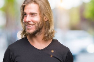 Yakışıklı delikanlı uzak tarafına yüzünde, doğal ifade gülümseme ile seyir izole arka plan üzerinde uzun saçlı. Kendine güvenen gülüyor.