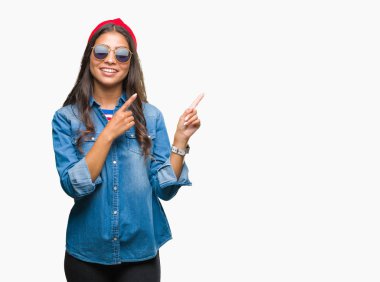 Genç güzel Arap kadın gülümseyerek ve iki elleri ve parmakları ile tarafına işaret kamera bakarak izole arka plan üzerinde güneş gözlüğü takıyor.