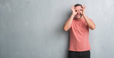 Beyaz delikanlı, dilini parmaklarının arasından baktığını yapışmasını dürbün gibi ok jest yapıyor gri grunge duvarın üzerinden. Deli ifade.