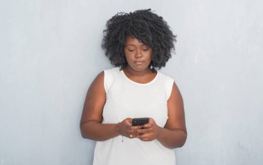 Acımak yüz ciddi düşünüyorum üstünde emin ifade ile smartphone kullanarak gri grunge duvar manifatura iletisi genç Afro-Amerikan kadın