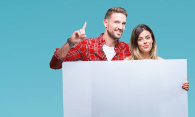 Boş bir arada tutan genç çift izole arka bir fikirle sürpriz üzerinde banner veya gülen yüz, bir numara ile işaret parmağı soru